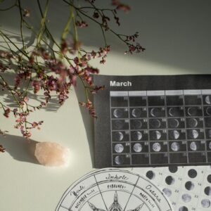 Aesthetic top view of a moon phases calendar with crystals and flowers on a desk.